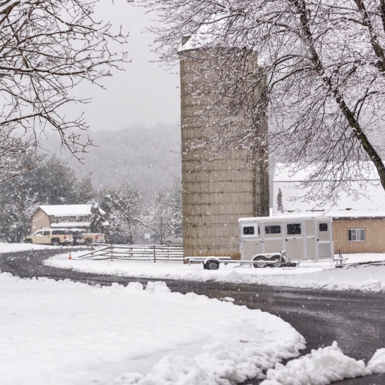 A snowy farm scene with a silo and horse trailer
