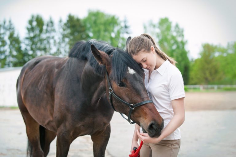 A girl resting her head on her horse's head.