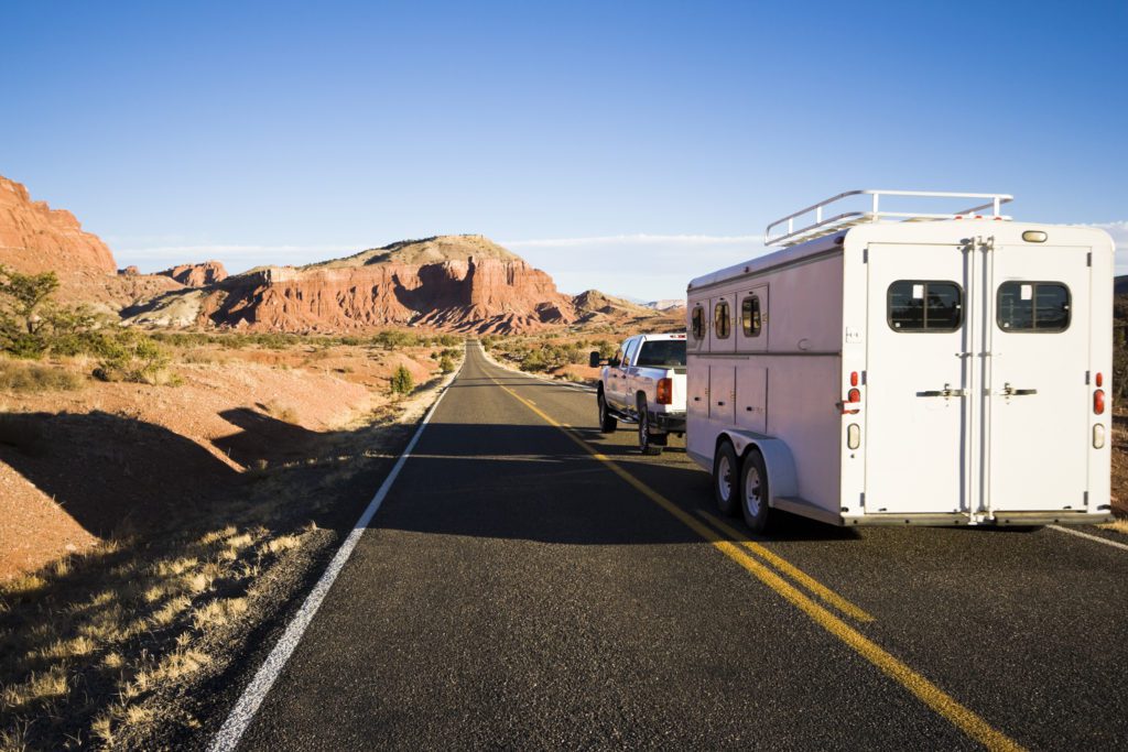 A horse trailer doing down a highway in a desert setting