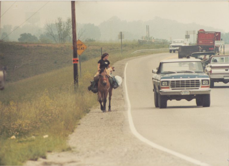 A woman riding a horse down the side of a highway
