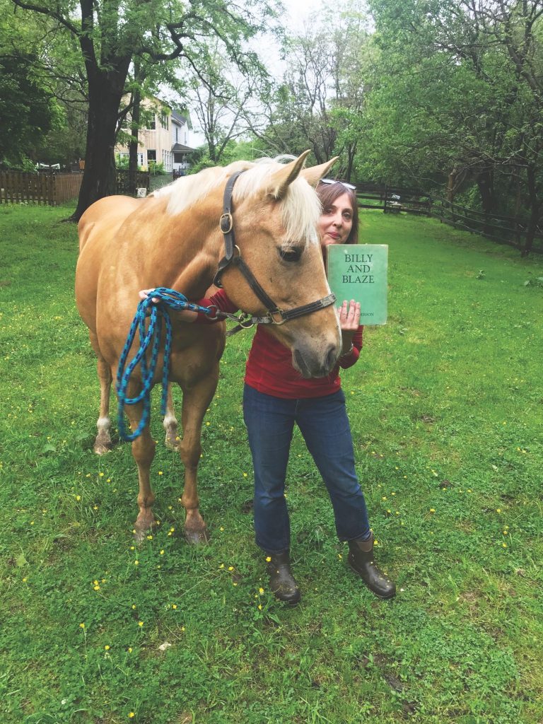 Woman standing with palomino horse and holding up copy of book