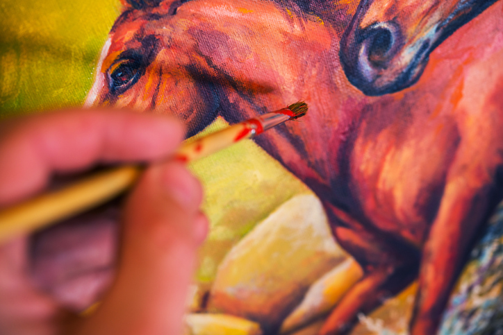 Hand holding paintbrush over painting of horse