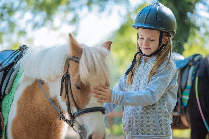 child in helmet petting spotted pony