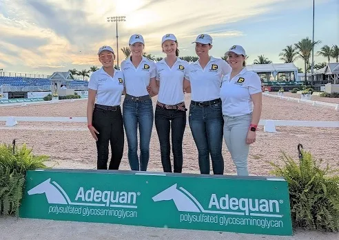 Group of 4 young dressage riders stand on podium behind Adequan sponsorship sign