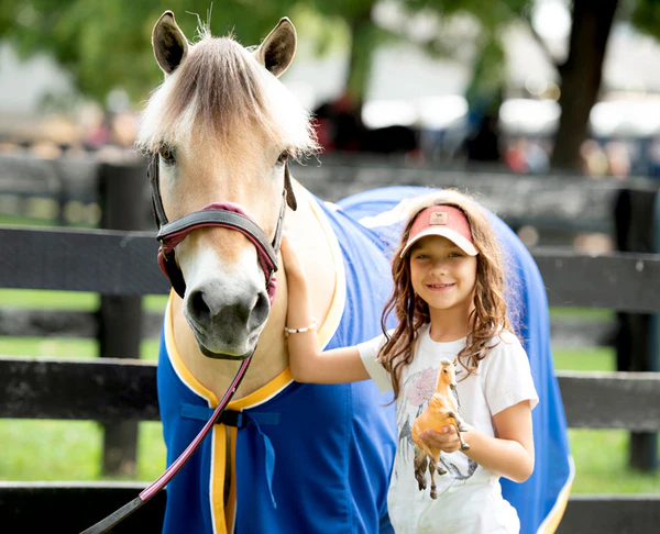 Smiling young girl holds a model horse in one hand and a real horse in the other