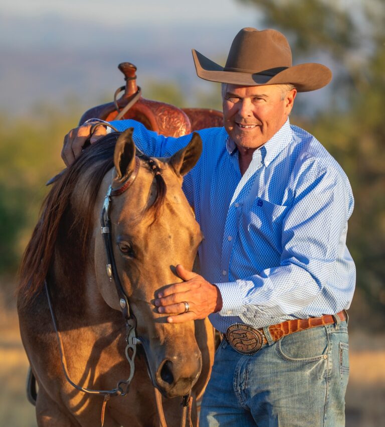 Horseman with Western hat standing alongside horse wearing Western saddle