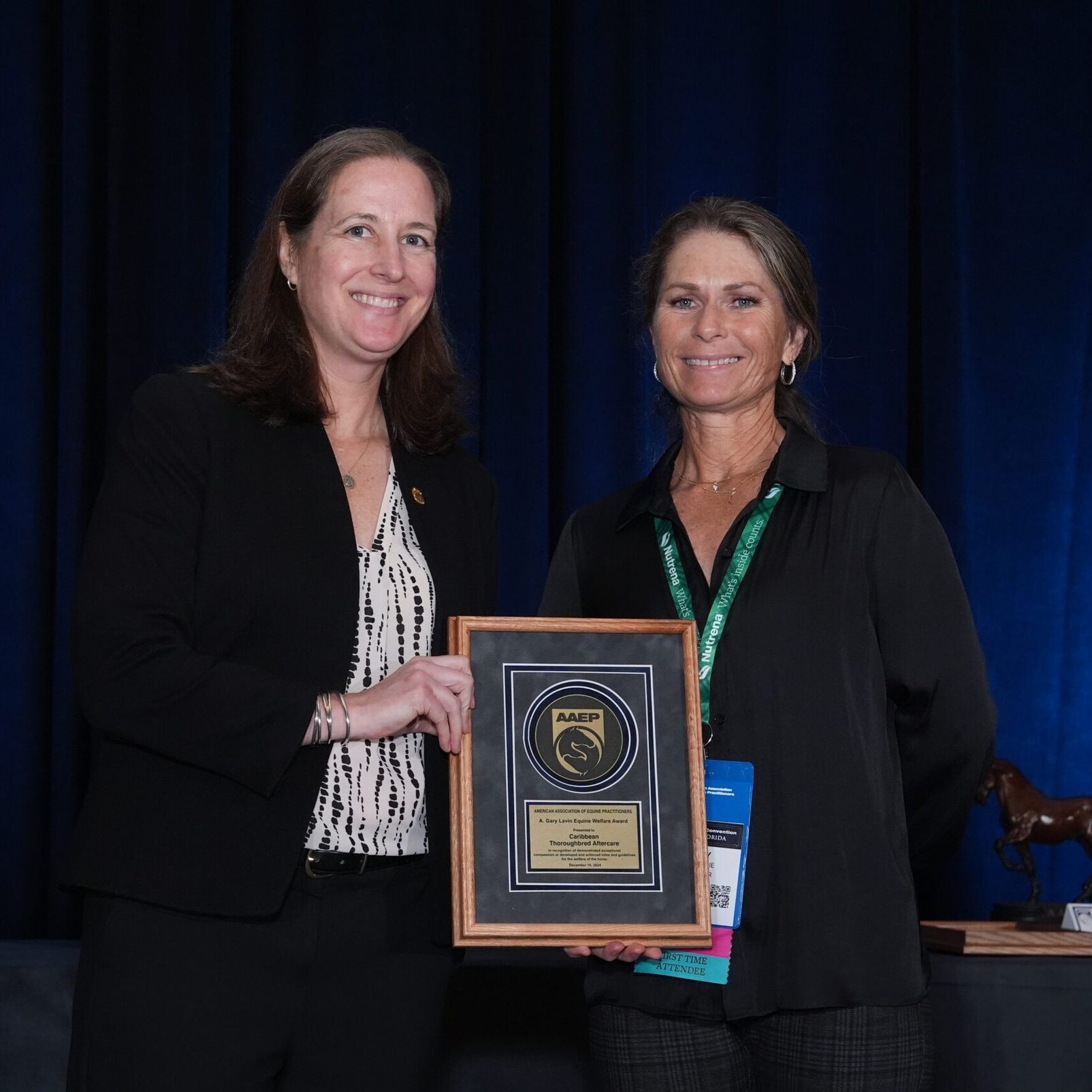 A woman presenting an AAEP award plaque to another woman