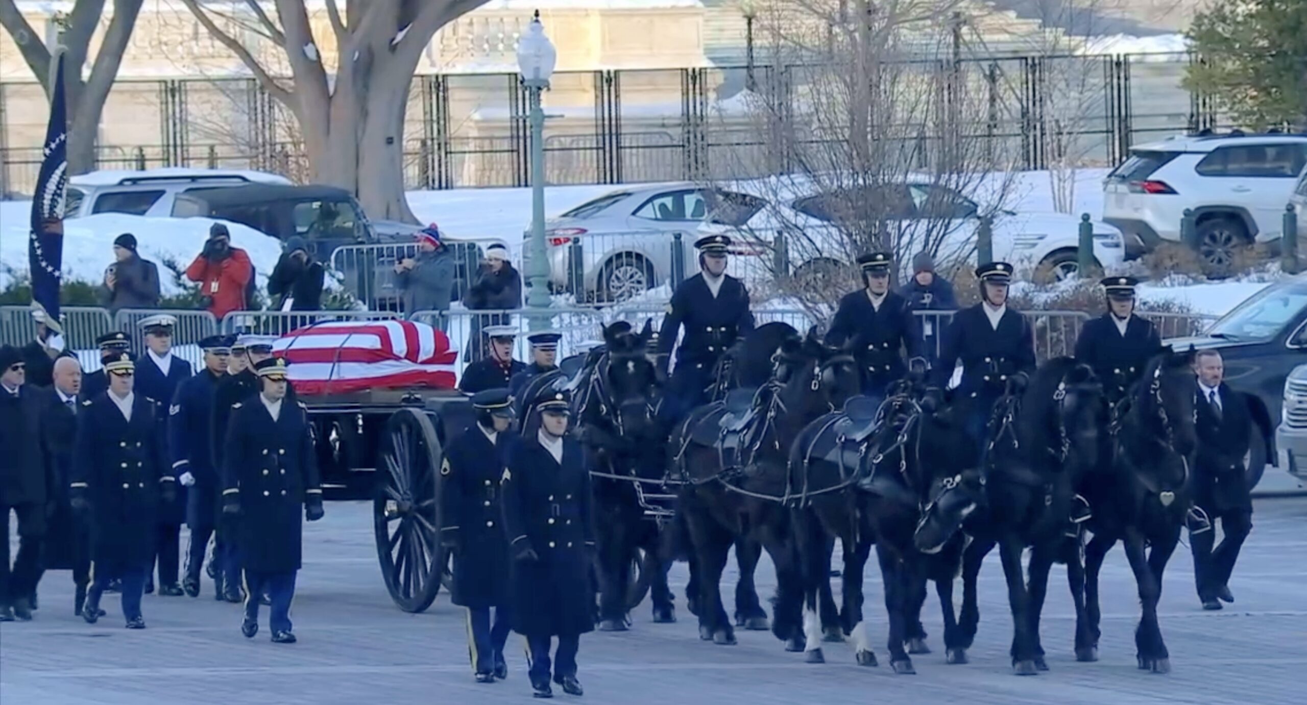 A team of black horses drawing a funeral caisson with a flag-draped coffin