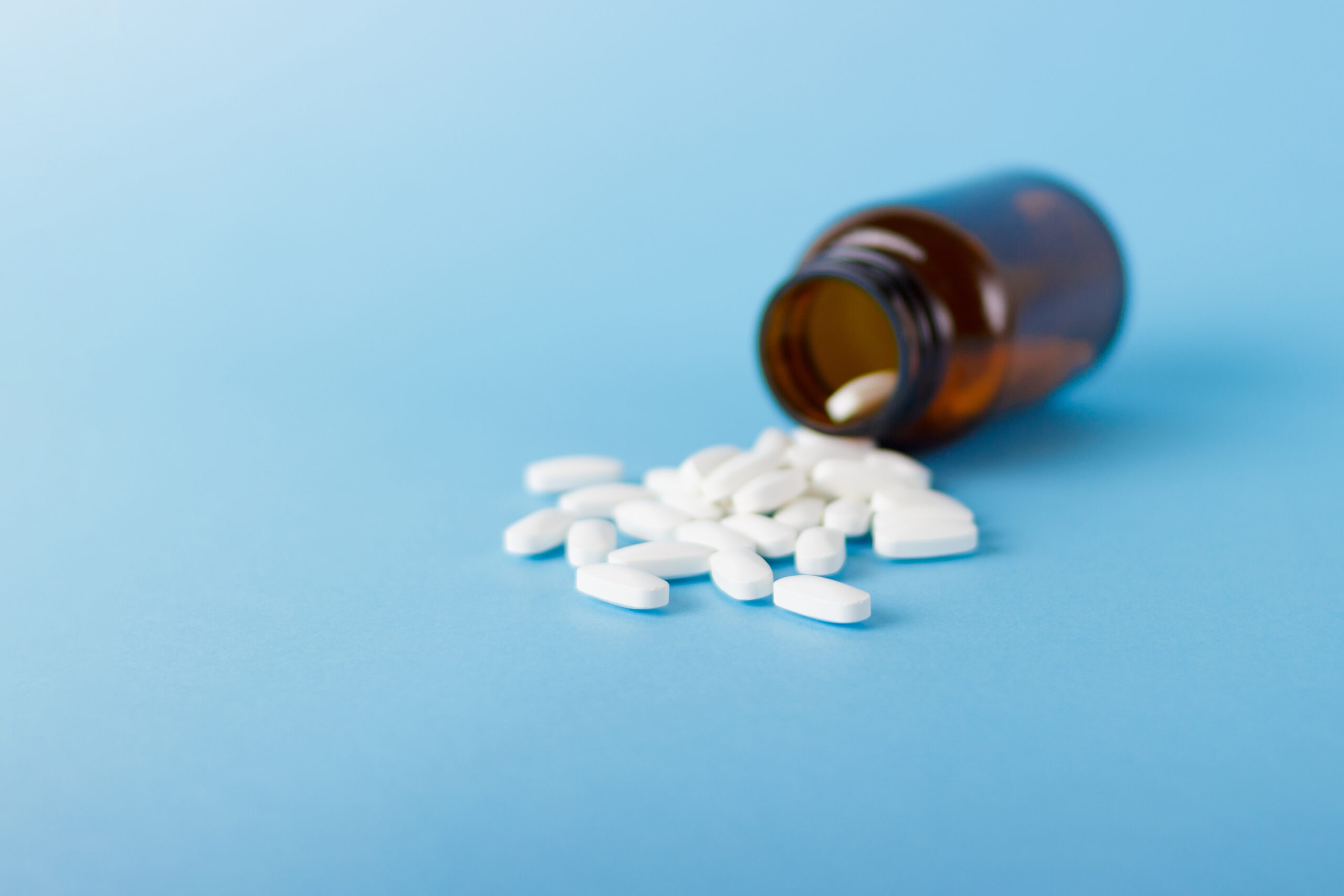 Close up white piils tablets vitamins in glass bottle jar isolated on blue background side view
