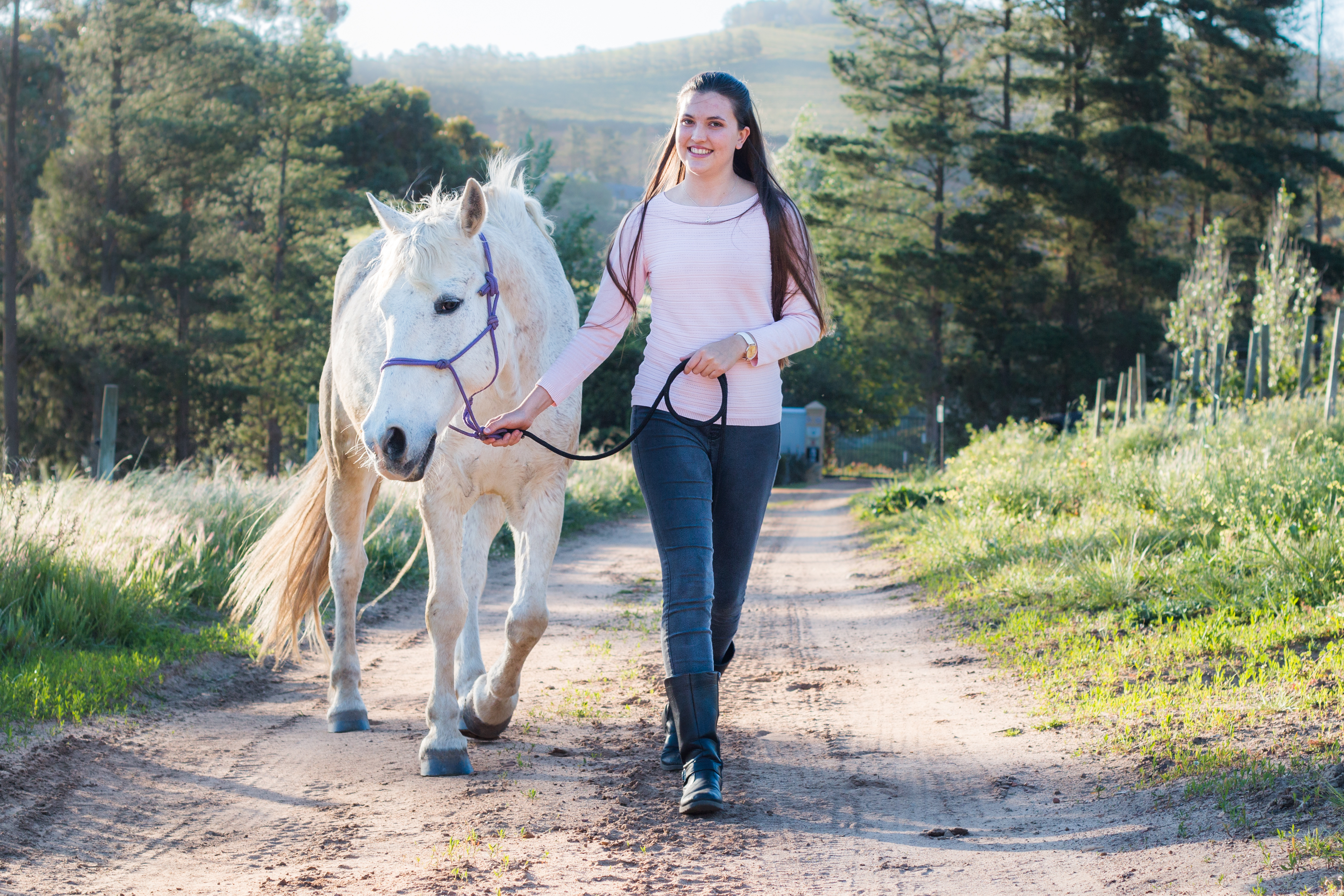 A girl walking a white horse down a dirt road