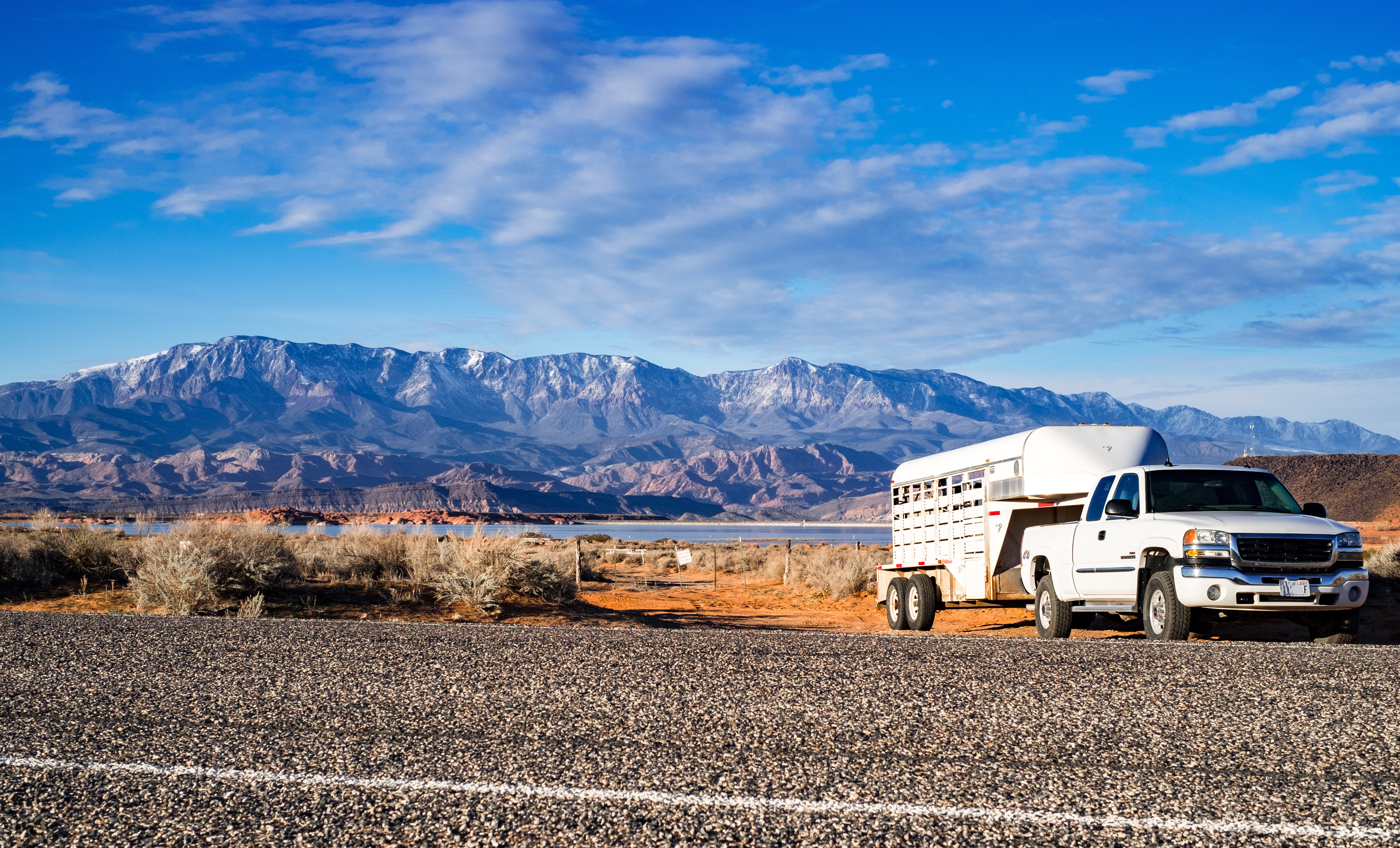 A horse trailer parked by the side of the road, with mountains in the background. 